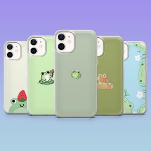 May include: A selection of phone cases featuring frog designs. The cases are in shades of green and white, with illustrations of frogs with flowers, reading books, and holding cups. The cases are displayed against a purple background.