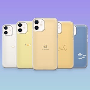 Peut inclure: Cinq coques de téléphone alignées, chacune avec un design différent. Les coques sont blanches, jaunes, jaune clair et bleues. Les motifs incluent un smiley, un visage de canard, un lever de soleil avec du texte, une scène de plage et des nuages.