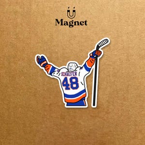 May include: A sticker depicting a hockey player in a white, blue, and orange jersey with the number 48. The player is holding a hockey stick above their head. The word "Magnet" is printed above the sticker.