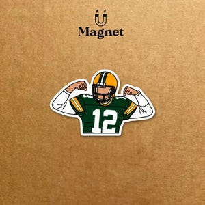 May include: A sticker featuring a football player in a green and yellow uniform with the number 12. The player is flexing his arms. The word "Magnet" is above the image.