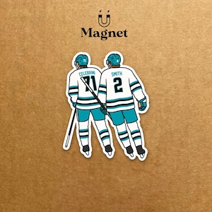 Könnte beinhalten: Ein Magnet mit zwei Eishockeyspielern in türkis-, schwarz- und weißfarbenen Uniformen. Die Spieler sind von hinten zu sehen, mit den Namen "CELEBRINI" und "SMITH" und den Nummern "71" und "2". Das Wort "Magnet" steht über dem Bild.