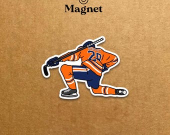 May include: A sticker magnet featuring a hockey player kneeling on one knee, holding a hockey stick. The player wears an orange and blue uniform with the number 20. The word "Magnet" is above the image.