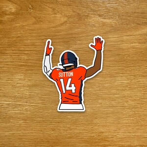 May include: A die-cut sticker featuring a football player seen from behind, wearing an orange jersey with the name SUTTON and the number 14 in white. The player wears a dark helmet and orange gloves with both arms raised in a celebratory gesture.