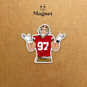 Puede incluir: Un imán con una ilustración de dibujos animados de un jugador de fútbol americano con una camiseta roja con el número 97. El jugador lleva un casco y tiene los brazos levantados con las manos abiertas. La palabra "Magnet" está arriba.