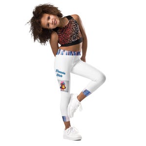May include: A child wearing a two-piece athletic set. The top is a leopard print sports bra. The white leggings have a blue and white plaid waistband and ankle cuffs. The leggings feature a cartoon bird graphic with the text "Bunnia Bird".