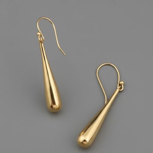 May include: A pair of gold-colored teardrop earrings. The earrings have a smooth, polished finish and a simple hook design. The teardrop shape is elongated and slightly rounded at the bottom, creating a sleek and elegant look.