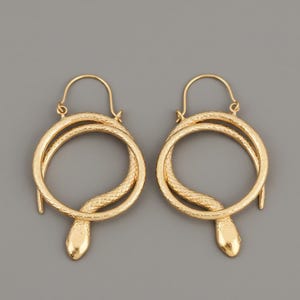 Peut inclure: Une paire de boucles d'oreilles créoles dorées. Chaque boucle d'oreille présente un motif de serpent enroulé autour d'un cercle, avec la tête du serpent en bas. Les boucles d'oreilles ont une surface texturée et une fermeture à crochet.