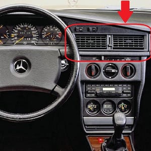 Puede incluir: Panel de instrumentos de un coche clásico, con volante negro, indicadores y consola central con rejillas de ventilación y controles. El salpicadero tiene un acabado de veta de madera y un reloj digital.