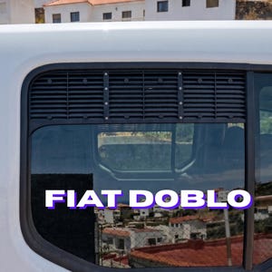 Peut inclure: Gros plan sur la fenêtre d'un véhicule blanc avec le texte "FIAT DOBLO" en blanc avec un contour violet. La fenêtre a une grille noire en haut et reflète une vue de bâtiments.