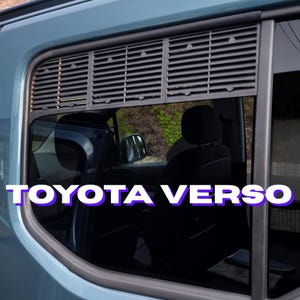 Peut inclure: Gros plan sur une vitre de voiture avec un pare-soleil à lamelles grises. Le texte "TOYOTA VERSO" est affiché en blanc avec un contour violet. L'intérieur de la voiture est visible.