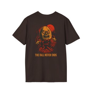 May include: A brown t-shirt with a spooky cartoon egg character design. The illustration includes a red sun, forest, and the text "THE FALL NEVER ENDS". The egg character has an angry expression and a red bow tie. A Halloween-themed graphic.