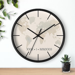 May include: A round wall clock with a black frame. The clock face features a world map design in neutral tones. Black hands and hour markers contrast against the map. The text "XXIX • I • MMXXIII" is printed at the bottom.