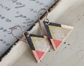 May include: A pair of geometric triangle earrings with a gold, black, white, and pink color scheme. The earrings have a textured, glittery finish.