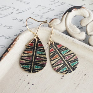 May include: A pair of gold teardrop earrings with a black background and colorful geometric pattern. The earrings have a sparkly finish.