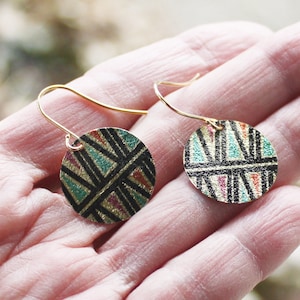 May include: A pair of gold hoop earrings with a black, teal, and pink geometric pattern.