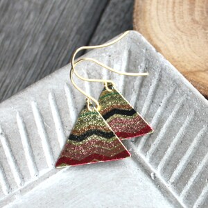 May include: A pair of gold triangle earrings with a red, black, gold, and green geometric pattern.
