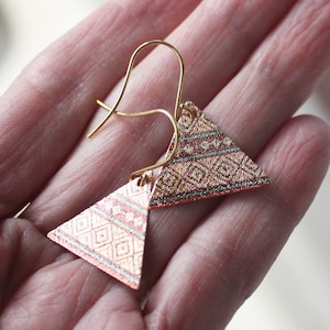 May include: A pair of gold triangle earrings with a pink and green geometric pattern. The earrings have a shiny, metallic finish.