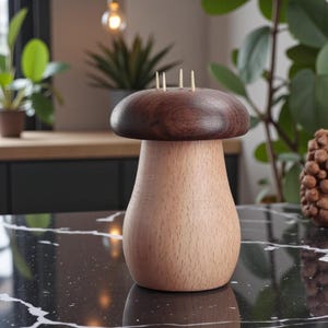 Puede incluir: Un palillero de madera con forma de hongo. La parte superior es de color marrón oscuro y el cuerpo es de color marrón claro. Se ven tres palillos en la parte superior. El soporte está sobre una superficie moteada en blanco y negro.