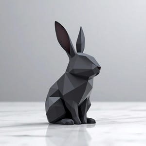 Puede incluir: Escultura geométrica negra de un conejo con diseño facetado. El conejo está sentado, con orejas largas y una pequeña nariz roja. La escultura está hecha de un material mate y se encuentra sobre una superficie blanca.
