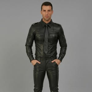 May include: A black leather long-sleeve button-down shirt with a matching black leather tie, featuring two chest pockets with flaps, shoulder epaulets, and a pointed collar, paired with matching black leather trousers with side pockets.