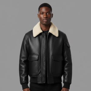 Puede incluir: Chaqueta bomber de cuero negro con cuello de borrego color crema. La chaqueta tiene dos bolsillos delanteros, cierre de cremallera y dobladillo acanalado. El modelo lleva una camisa negra debajo.