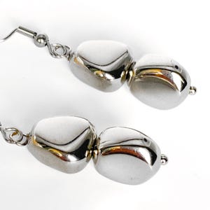 May include: A pair of silver-colored earrings. Each earring features three polished, rounded beads connected by small metal loops. The earrings have a fish hook style closure.