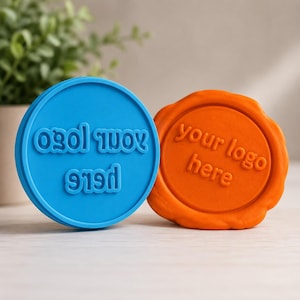May include: A circular blue stamp and a circular orange stamp, both featuring the embossed text 'your logo here'. The blue stamp has a smooth, defined edge, while the orange stamp has an irregular, wax-seal style textured border.