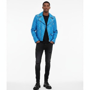 Op de afbeelding: Een blauwe leren jas met een wit patroon, gedragen over een zwart t-shirt en zwarte jeans. De jas heeft een klassieke biker-stijl met een reverskraag en asymmetrische rits. Het model draagt zwarte laarzen.