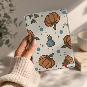 May include: A clear tablet case featuring a repeating pattern of orange pumpkins, a single blue gourd, and small green vines on a cream background. The design is accented with scattered blue, green, and red polka dots across the surface.