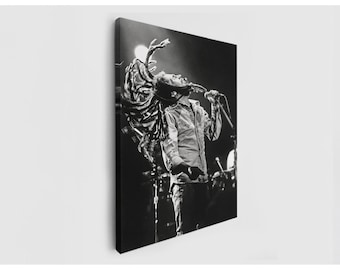May include: Black and white canvas print of a musician performing on stage. The image captures the musician mid-performance, with his arms raised and a microphone in front of him. The background is dark, with stage lights illuminating the performer.