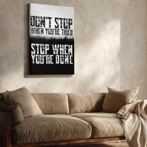 a motivational poster with the text "Don't Stop When You're Tired" and "Stop When You're Done" displayed on a wall above a beige couch.