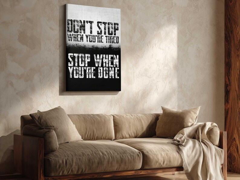 a motivational poster with the text "Don't Stop When You're Tired" and "Stop When You're Done" displayed on a wall above a beige couch.
