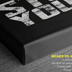 a close-up view of a black canvas or frame with a white text design on it. The text design appears to be a stylized phrase or message, and the image is described as a "ready to hang" piece of art.