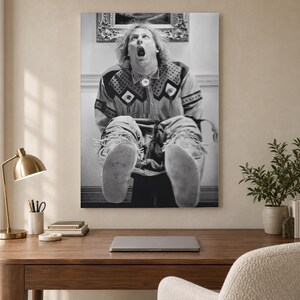 May include: A black and white wall art print featuring a person with long hair, mouth open in an expression of shock, wearing a long-sleeved shirt with a patterned yoke and fringe details, paired with light-colored moccasin-style footwear.