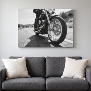 May include: A black and white wall art print featuring a motorcycle in motion on a paved road. The image captures the front wheel, engine, and handlebars of the bike, with a blurred background suggesting speed and movement along a highway.