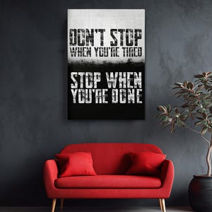 a motivational poster with the text "DON'T STOP WHEN YOU'RE TIRED STOP WHEN YOU'RE DONE" displayed on a wall above a red sofa.