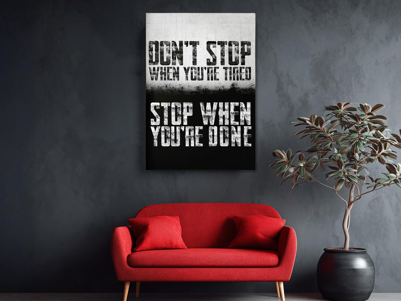 a motivational poster with the text "DON'T STOP WHEN YOU'RE TIRED STOP WHEN YOU'RE DONE" displayed on a wall above a red sofa.
