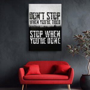 a motivational poster with the text "DON'T STOP WHEN YOU'RE TIRED STOP WHEN YOU'RE DONE" displayed on a wall above a red sofa.