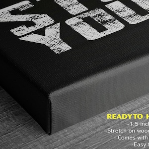 a close-up view of a black canvas or frame with a white text design on it. The text design appears to be a stylized phrase or message, and the image is described as a "ready to hang" piece of art.