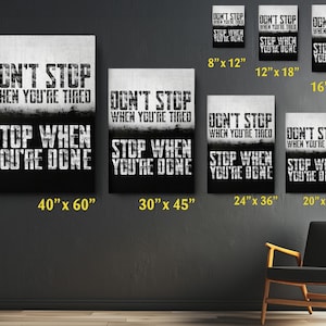 a collection of motivational posters with the text "DON'T STOP WHEN YOU'RE TIRED" displayed on them. The posters vary in size, with some being larger than others, and are arranged on a wall. There is also a chair in the background, suggesting a space for relaxation or contemplation.