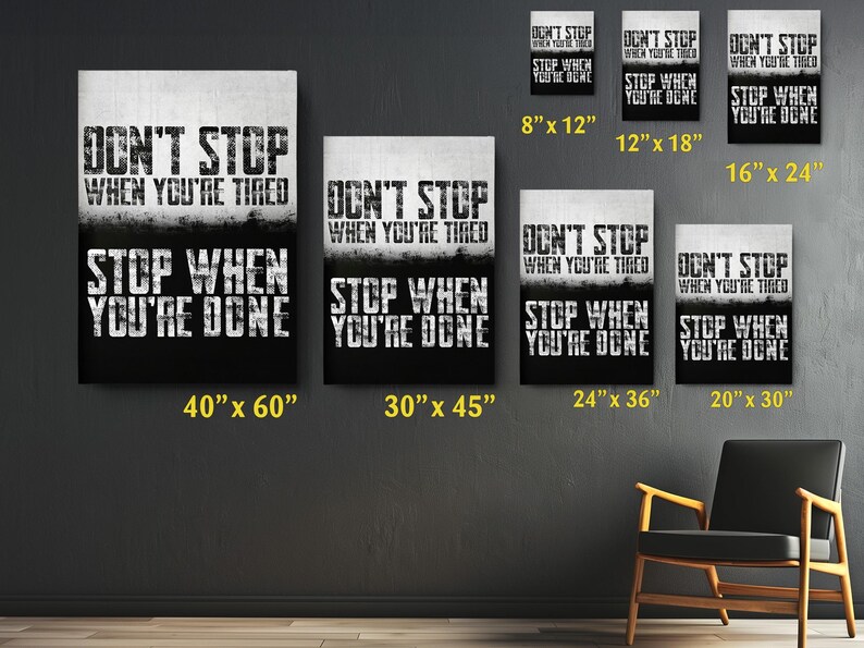a collection of motivational posters with the text "DON'T STOP WHEN YOU'RE TIRED" displayed on them. The posters vary in size, with some being larger than others, and are arranged on a wall. There is also a chair in the background, suggesting a space for relaxation or contemplation.