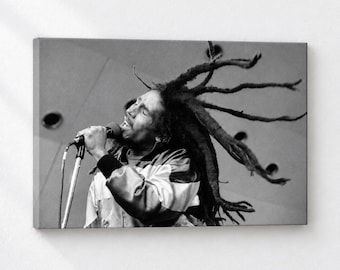 May include: A black and white photograph of a person with long dreadlocks singing into a microphone. The individual is wearing a jacket and has their head tilted back with eyes closed, while their hair fans out dynamically behind them.