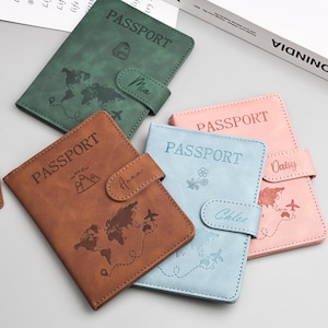 May include: A collection of passport holders in various colors: brown, green, blue, and pink. Each holder is embossed with the word "PASSPORT", a world map, and a name. The holders have a snap closure.