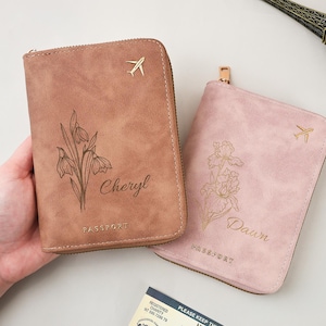 May include: Two personalised passport holders in pink and brown. The brown one has a floral design and the name "Cheryl", the pink one features a different floral design and the name "Dawn". Both have a gold airplane emblem.