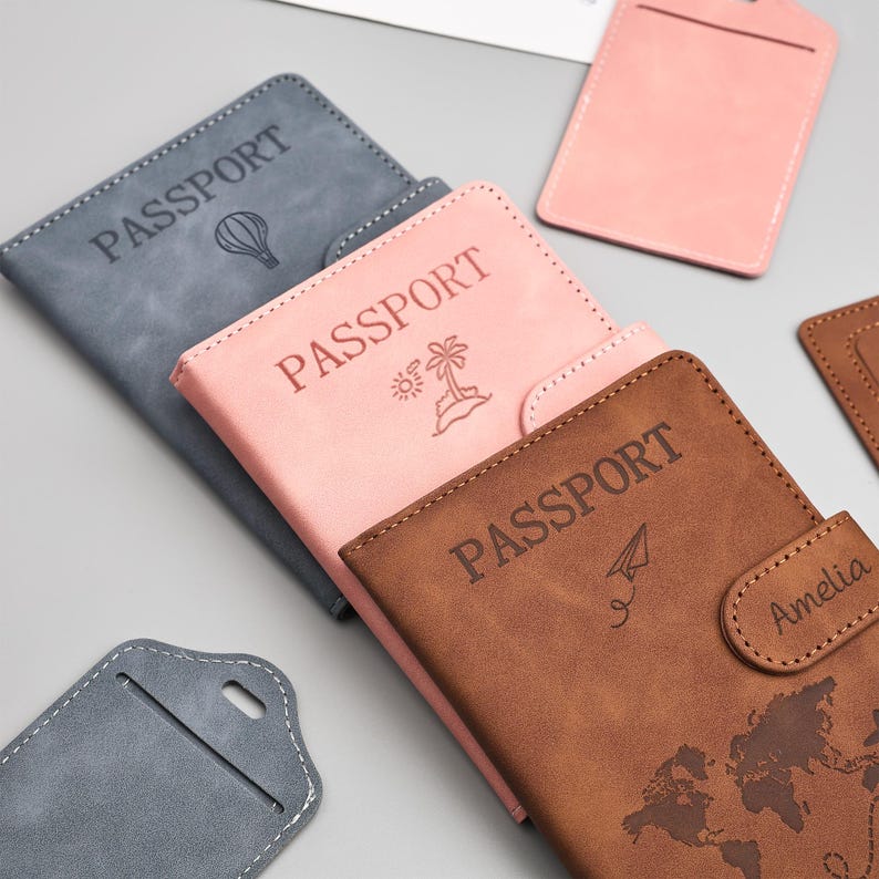 May include: A collection of passport holders in various colors, including gray, pink, and brown. Each holder is embossed with the word "PASSPORT" and a unique graphic, such as a hot air balloon, a palm tree, or a paper airplane. Some holders have a name on them.