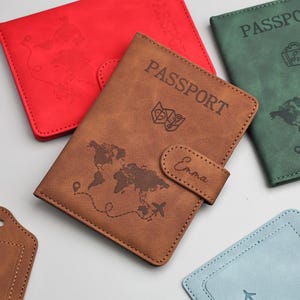 May include: A collection of passport holders in various colors, including red, brown, and green. The brown passport holder is in focus, featuring the word "PASSPORT" and a world map design. The name "Emma" is printed on the closure.