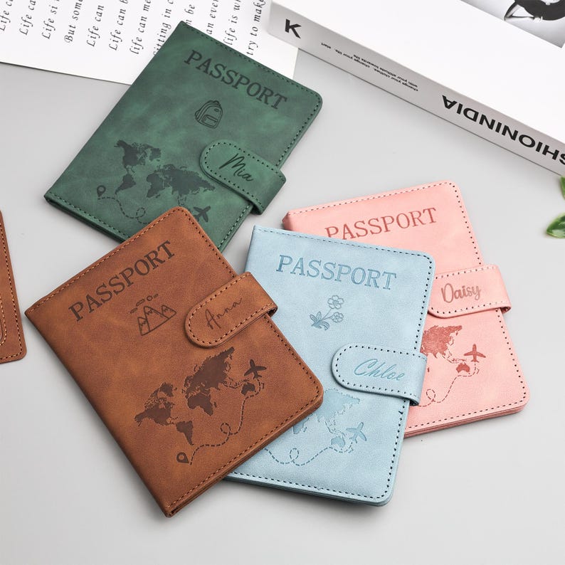 May include: A collection of passport holders in various colors: brown, green, blue, and pink. Each holder is embossed with the word "PASSPORT", a world map, and a name. The holders have a snap closure.