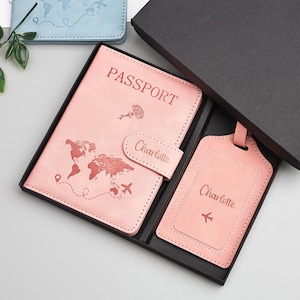 May include: A pink passport holder and luggage tag set in a black gift box. The passport holder features a world map design, the word "PASSPORT", and the name "Charlotte". The luggage tag also has the name "Charlotte" and an airplane icon.
