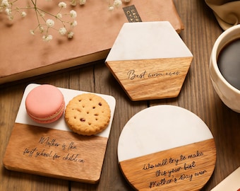 May include: A collection of wooden and marble coasters with engraved messages. One reads "Best mum ever", another "Mother is the first school for children", and the third "We will try to make this your best Mother's Day ever". A pink macaron and a biscuit are on one coaster.