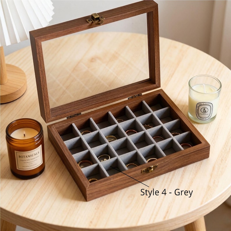 K&ouml;nnte beinhalten: Eine Holzschmuckschatulle mit Glasdeckel, ge&ouml;ffnet, um einen grauen Innenraum zu zeigen, der in kleine F&auml;cher unterteilt ist. Die Schatulle steht auf einem hellen Holztisch, mit einer Kerze und einer kleinen Glaskerze in der N&auml;he. Der Text "Style 4 - Grey" ist sichtbar.